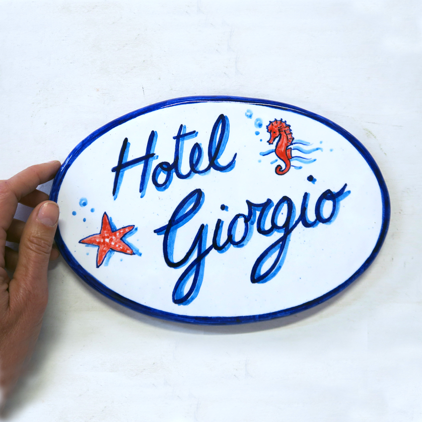 Produzione targhe e insegne fatte a mano. Targa, insegna in ceramica dipinta a mano ovale.
Disegno personalizzato su misura. Fatto a mano a Bologna.