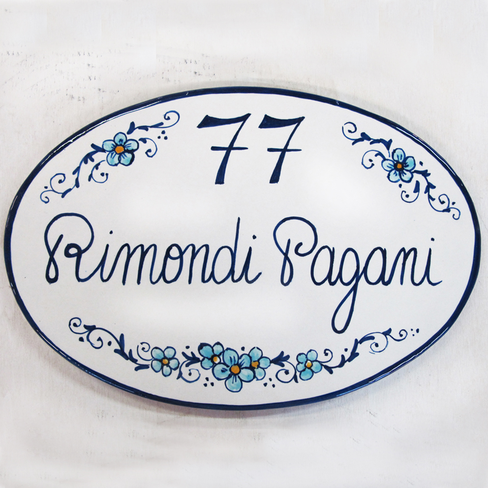 Targa ovale per la casa con Cognomi e numero civico e fiori in ceramica a Bologna Paese dei Balocchi. Targhe e numeri civici dipinti a mano. Decorazione ceramica personalizzata Ovale in maiolica 25 x 17 cm da esterno bianca e blu.